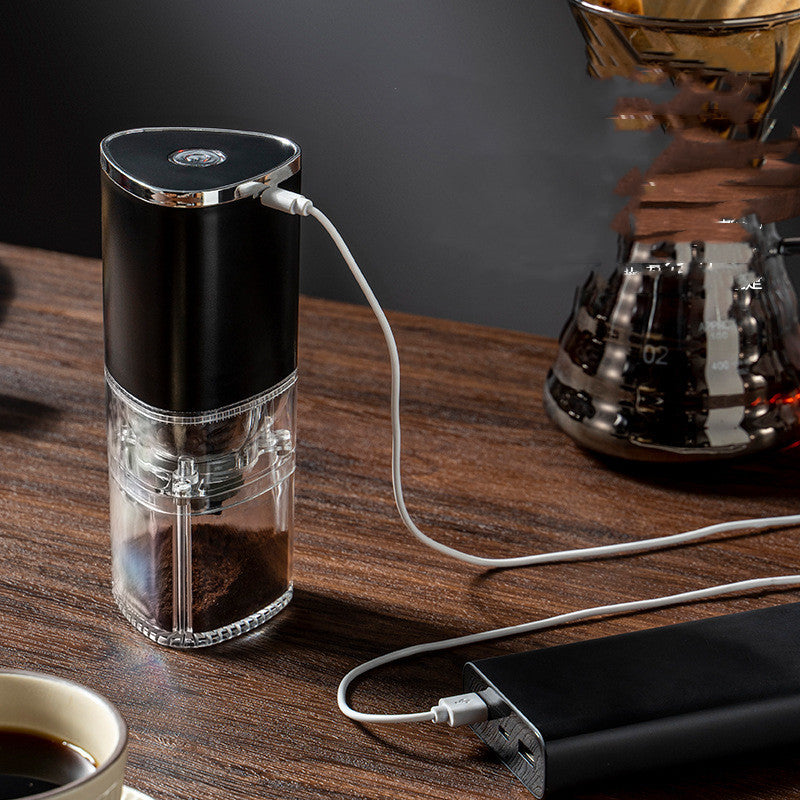 Electric coffee blade grinder charging on a wooden table with coffee and brewing equipment in the background.