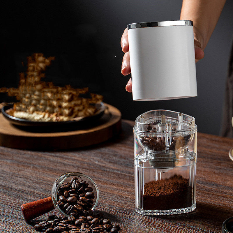 Electric coffee blade grinder in use with whole coffee beans and ground coffee on a wooden table.